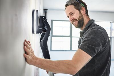 Vakman bewerkt muur met de Planex-langnek-schuurmachine met verlichting