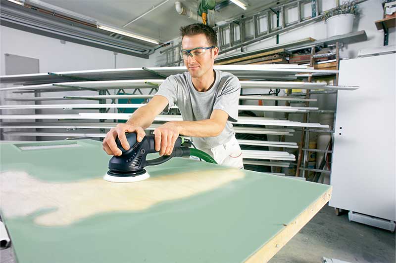 Een man schuurt een groen geverfd oppervlak