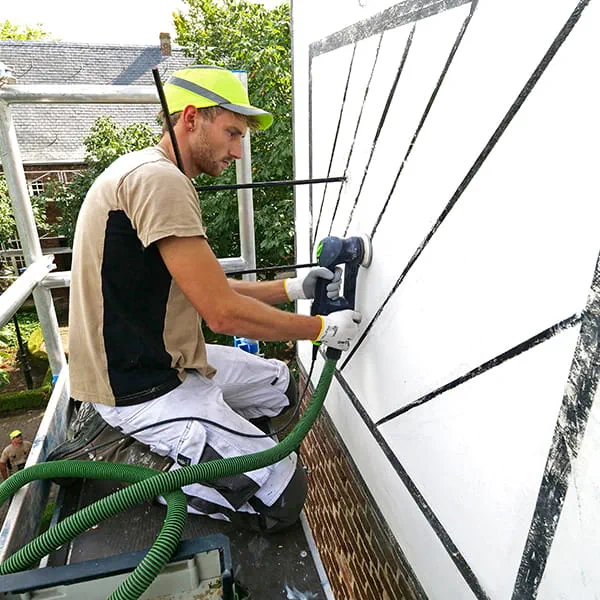 Een man werkt met een slijpmachine aan de gevel van het gebouw.