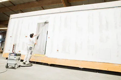De wanden van de prefabwoningen worden bewerkt met de langnek-schuurmachine van Festool.