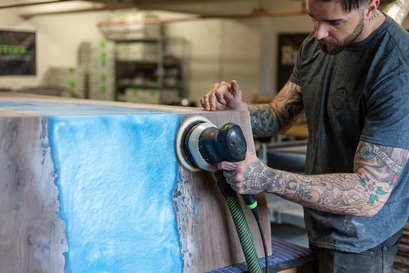 Het oppervlak van de 'River Table' wordt afgeschuurd met de Festool excenterschuurmachine