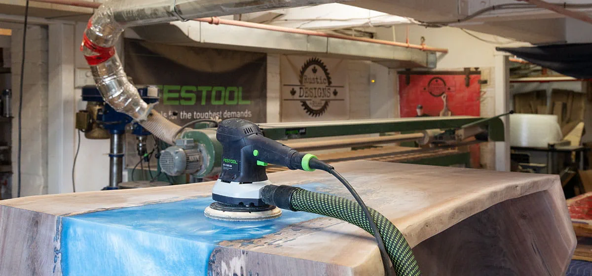 Het oppervlak van een 'River Table' wordt afgeschuurd met de Festool excenterschuurmachine
