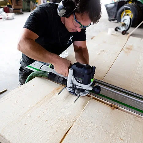 Een saunabouwer bij het bewerken van een oppervlak met een bovenfrees van Festool.