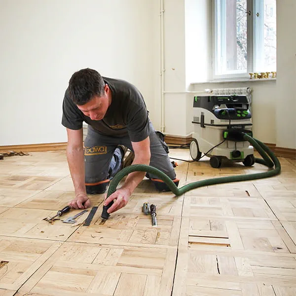 Meesterparketlegger Jarek Gawina maakt defecte delen in de parketvloer los en verwijdert ze met de mobiele stofzuiger van Festool